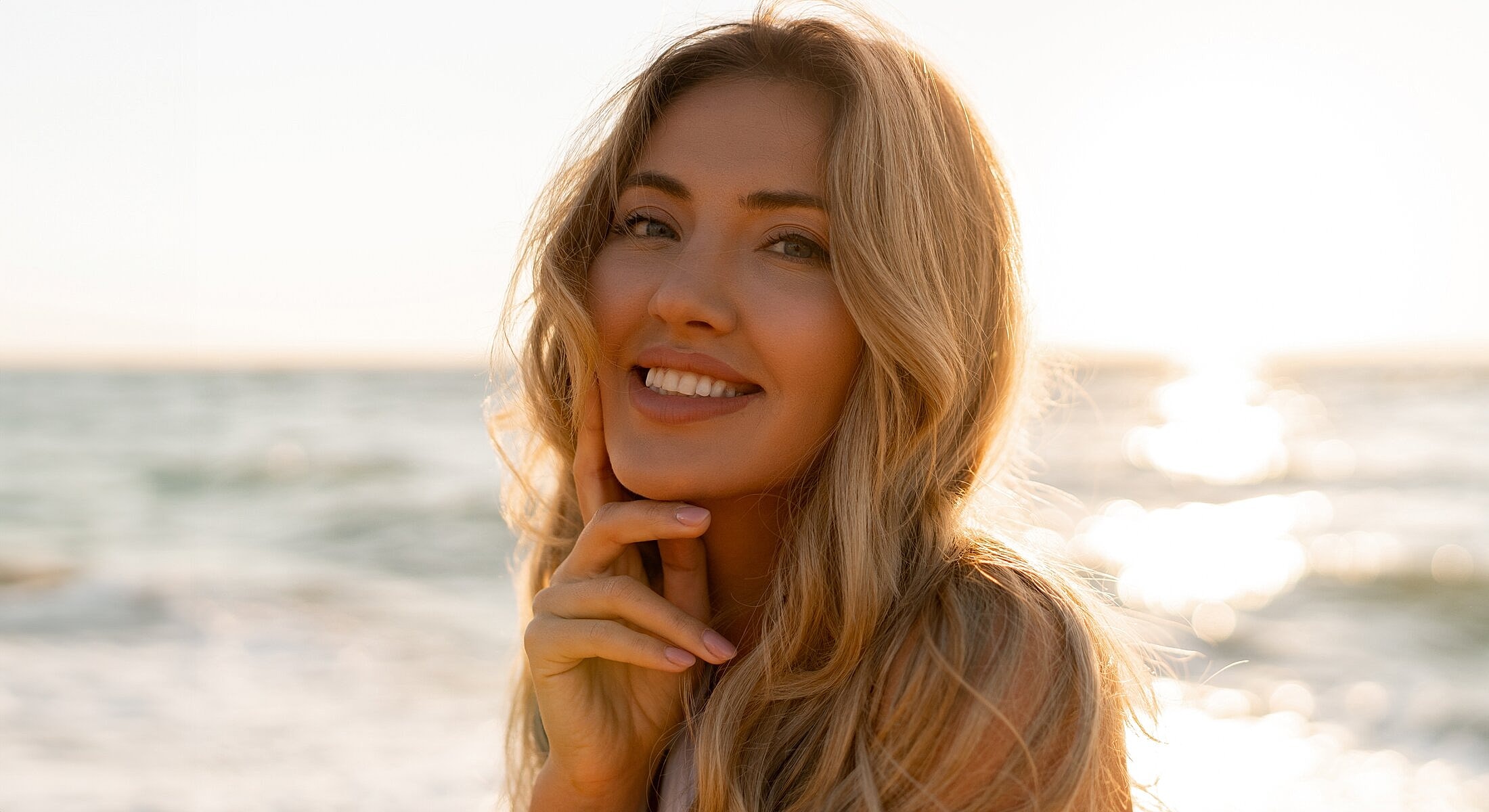 Smiling woman by the ocean at sunset.